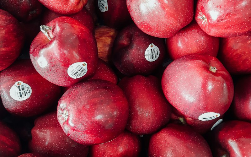A pile of shiny red apples, several with produce stickers